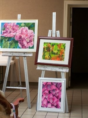 Three paintings are on display on white easels in the art hall